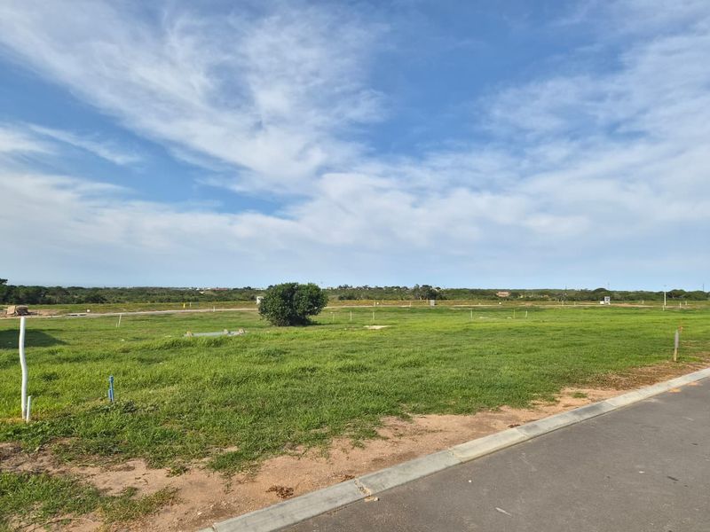 A vacant residential plot featuring a level grassed surface, paved road access, and established utility connection points in a quiet development area.