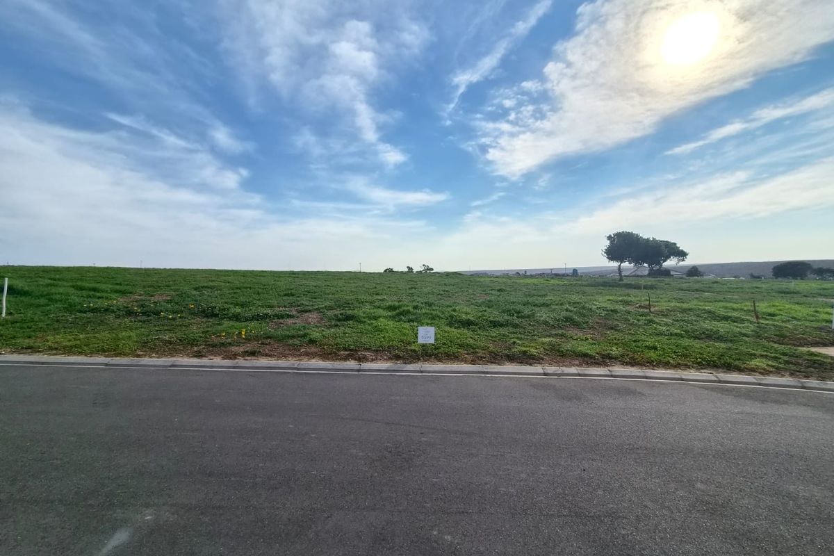 A vacant residential plot featuring a grassy landscape, accessible via a paved road, offering a clear view of the surrounding area.