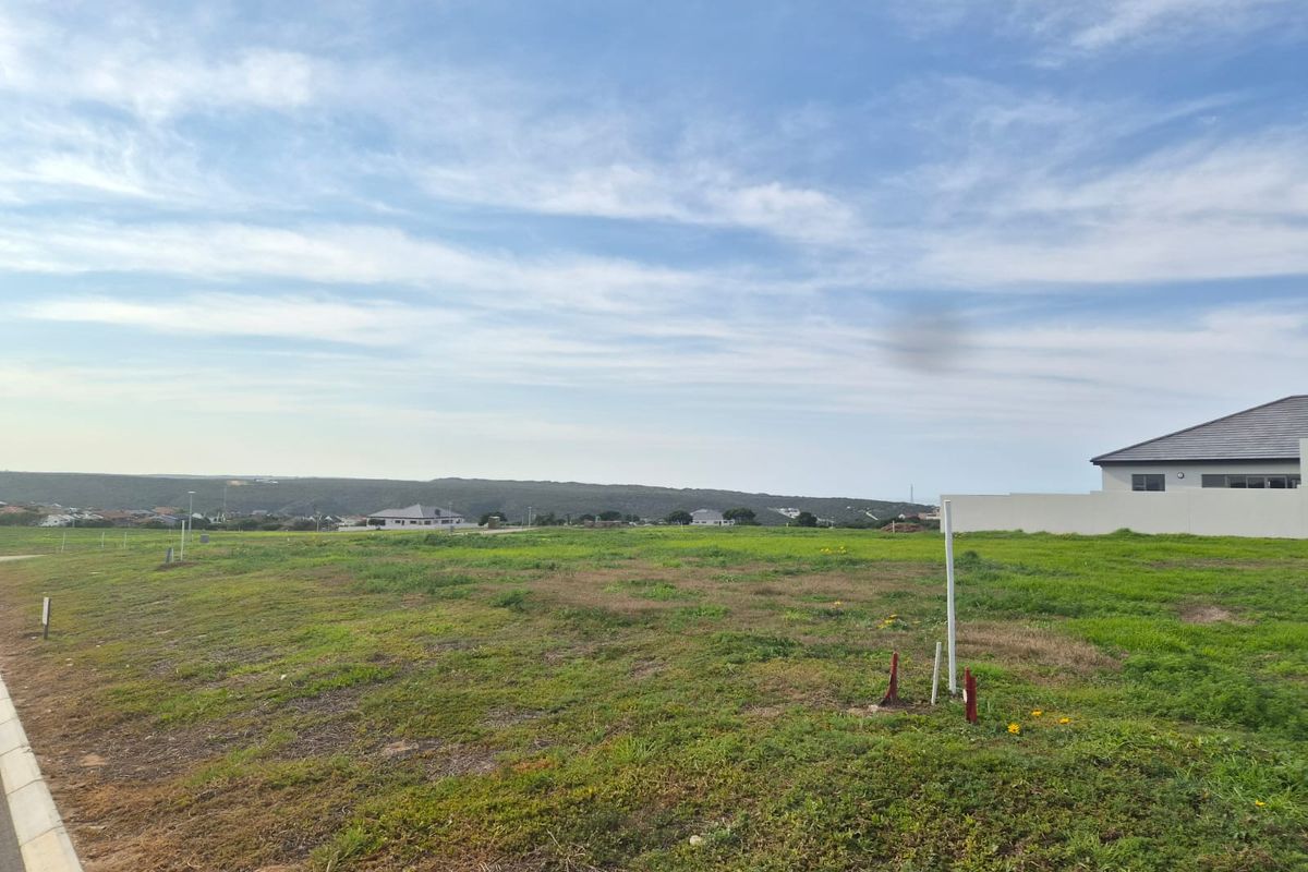 A vacant residential plot of land featuring open grass, boundary walling, and clear views of the surrounding neighborhood.