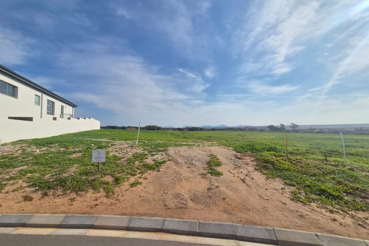 A vacant residential plot of land featuring a level building site with a paved curb and distant landscape views.