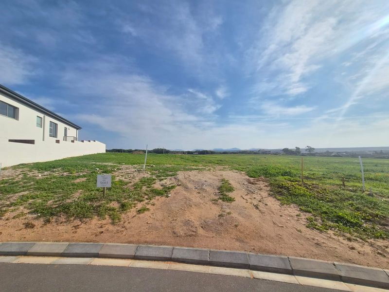 A vacant residential plot of land featuring a level building site with a paved curb and distant landscape views.