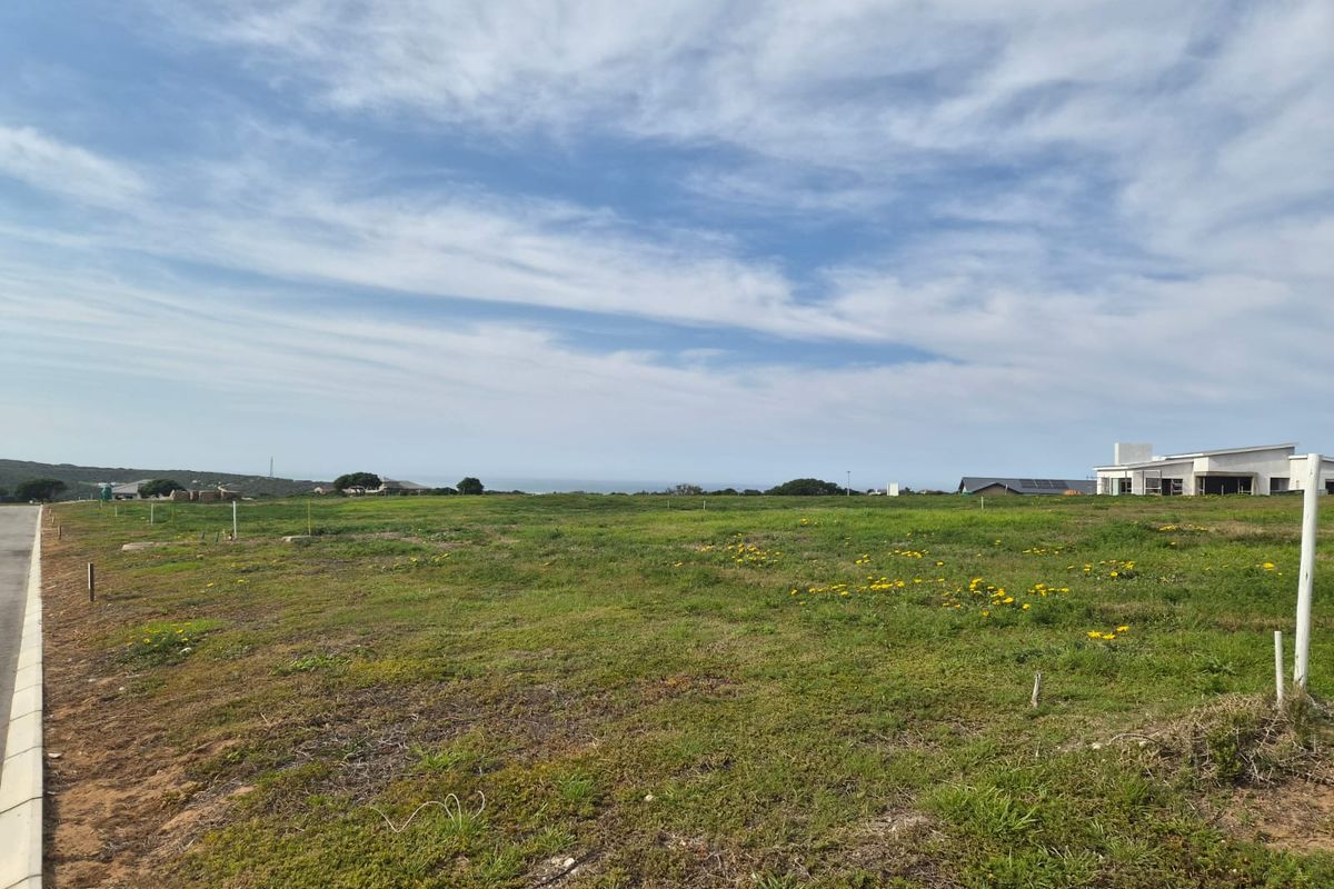 A vacant residential plot featuring a level grassy landscape with distant ocean views and adjacent modern housing developments.