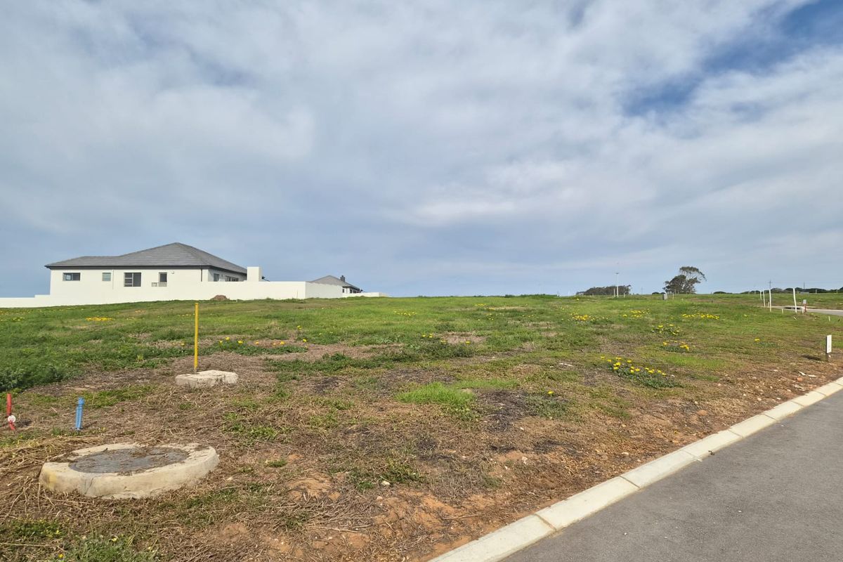 A vacant residential plot featuring a gentle slope, established road access, and visible utility connections, ready for development in a quiet neighborhood.