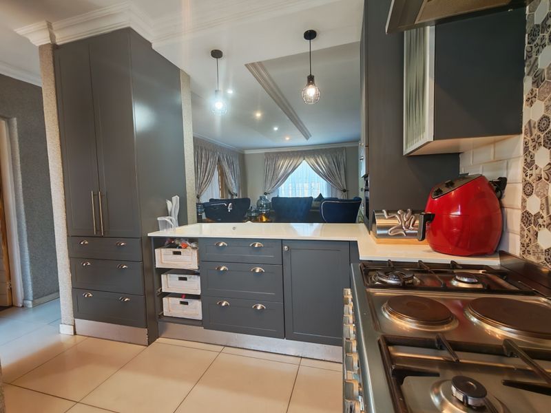 Modern kitchen featuring dark grey cabinetry, stone countertops, a gas hob, and stylish pendant lighting, seamlessly flowing into the adjacent living area.
