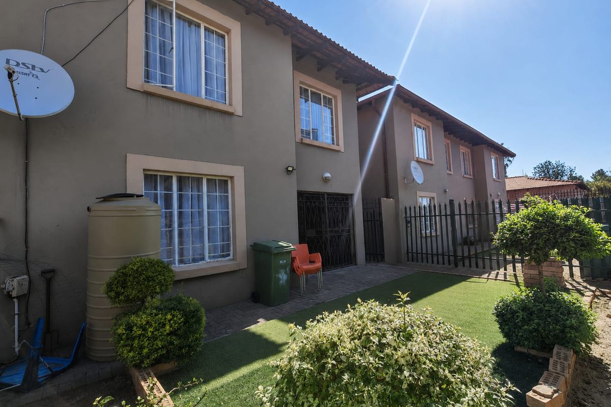 Rear view of the townhouse featuring a paved patio area, small garden, water tank, and secure metal fencing.