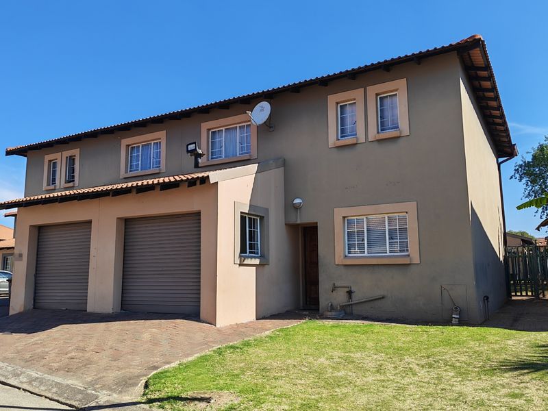 Front elevation of a double-story townhouse featuring a double garage, paved driveway, and a small front lawn area.