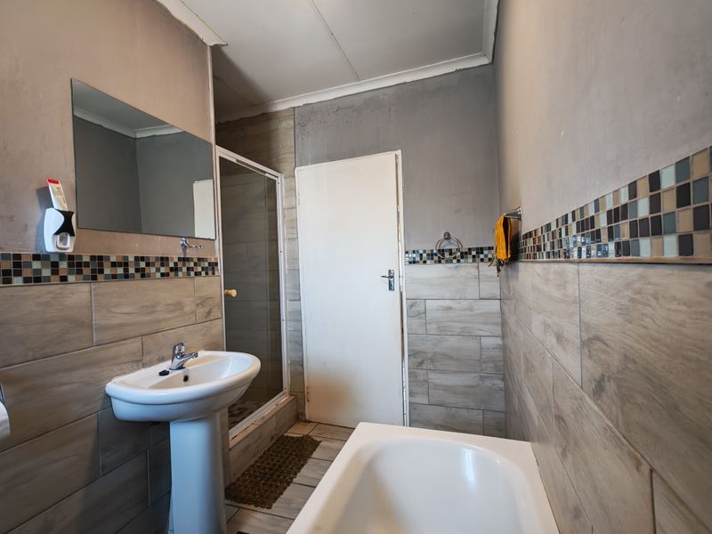 A functional bathroom featuring a pedestal basin, shower enclosure, and bathtub, finished with wood-look wall tiles and a decorative mosaic border.