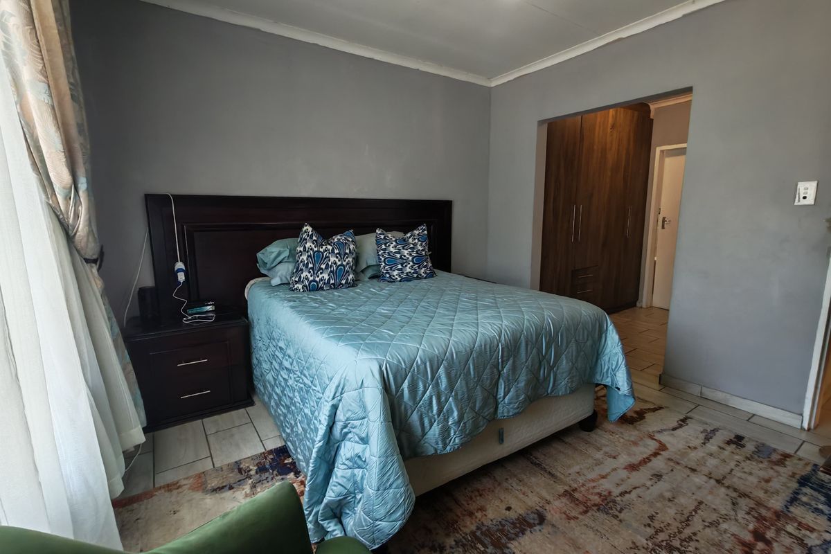 A spacious bedroom featuring built-in wooden cupboards, tiled flooring, and a ceiling fan, offering a functional layout with neutral wall tones.