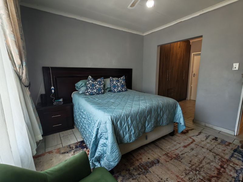 A spacious bedroom featuring built-in wooden cupboards, tiled flooring, and a ceiling fan, offering a functional layout with neutral wall tones.