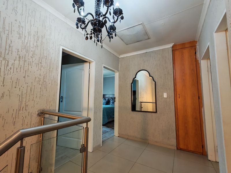 A bright upper-level hallway featuring tiled flooring, a modern glass and metal balustrade, and a built-in storage cupboard.