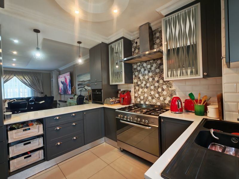 Modern open-plan kitchen featuring dark cabinetry, quartz countertops, gas stove, and decorative mosaic backsplash, seamlessly flowing into the adjacent living area.