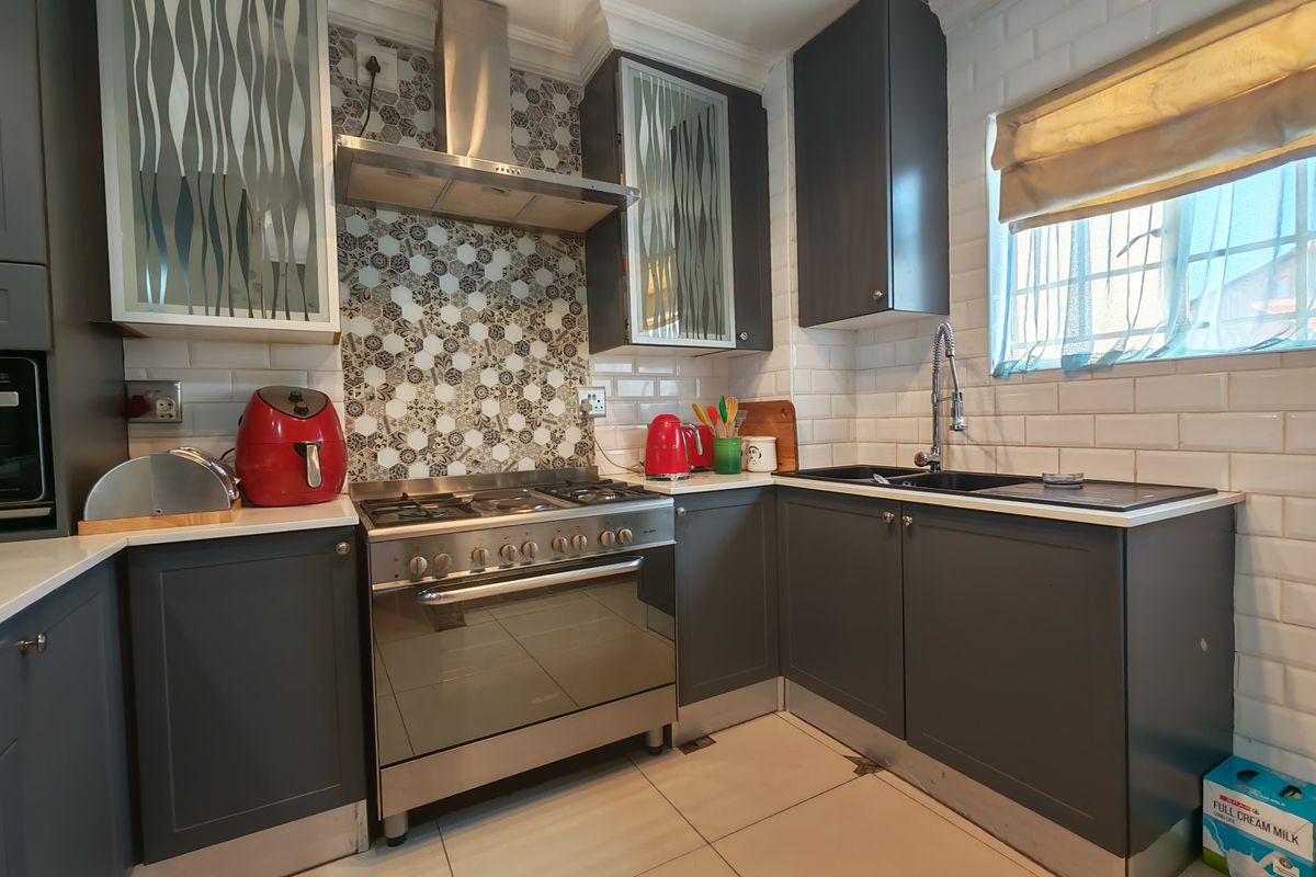 A modern kitchen featuring dark grey cabinetry, a gas stove with stainless steel extractor, subway tile backsplash, and a patterned feature wall.