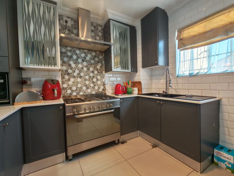 A modern kitchen featuring dark grey cabinetry, a gas stove with stainless steel extractor, subway tile backsplash, and a patterned feature wall.