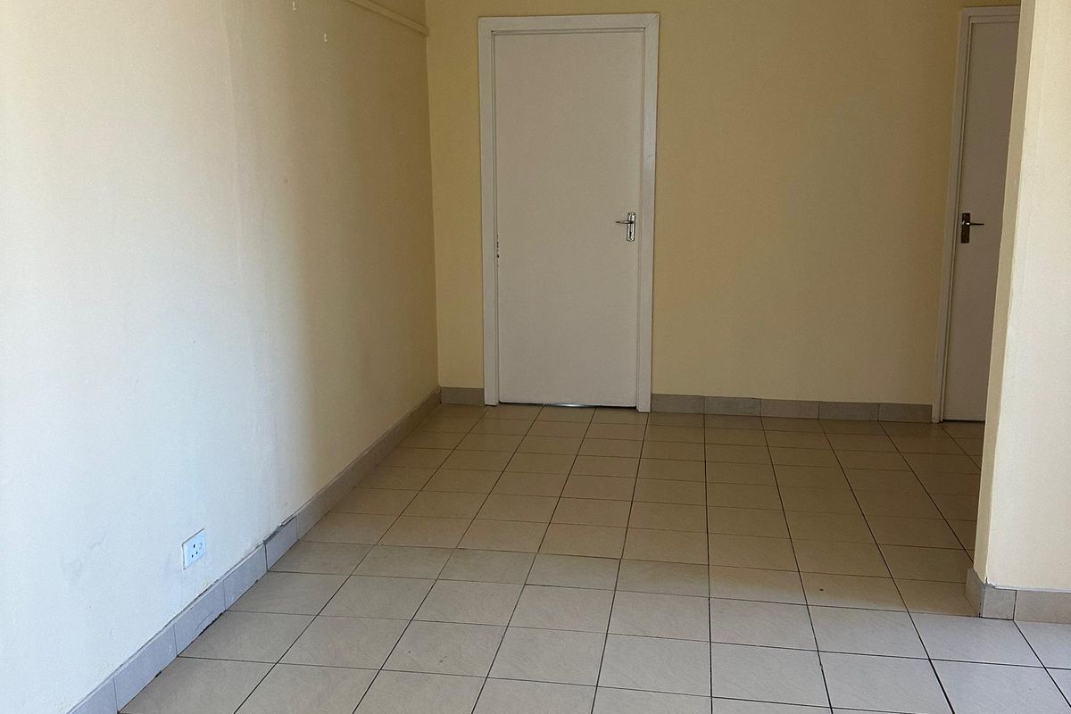 An empty living area featuring neutral tiled flooring, a ceiling fan, and plain walls, offering a blank canvas for interior design.