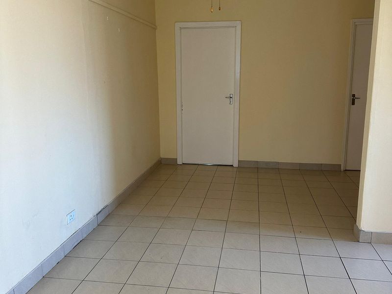 An empty living area featuring neutral tiled flooring, a ceiling fan, and plain walls, offering a blank canvas for interior design.