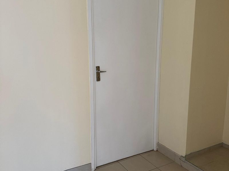 A simple, neutral-toned hallway featuring tiled flooring and a standard internal door, providing a clean and functional transition space within the apartment.