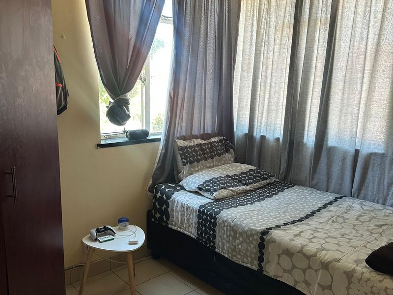 A compact bedroom featuring tiled flooring and a built-in cupboard, offering a functional space with natural light from the corner windows.