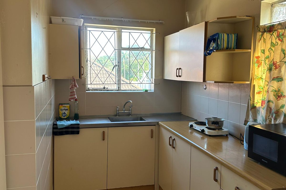 A compact kitchen featuring laminate countertops, built-in cabinetry, a stainless steel sink, and tiled flooring with a window providing natural light.