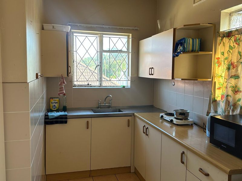 A compact kitchen featuring laminate countertops, built-in cabinetry, a stainless steel sink, and tiled flooring with a window providing natural light.