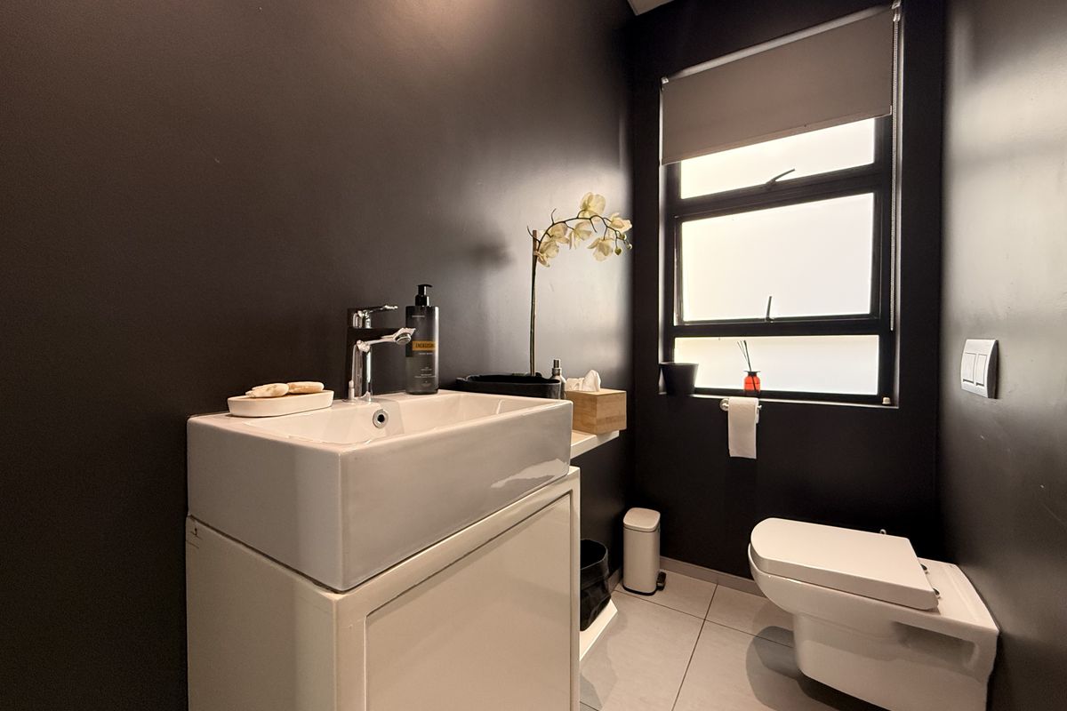 A modern guest bathroom featuring a sleek basin with vanity cabinet, wall-hung toilet, and dark feature walls.