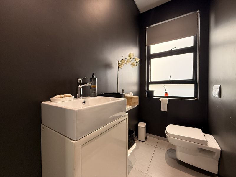 A modern guest bathroom featuring a sleek basin with vanity cabinet, wall-hung toilet, and dark feature walls.