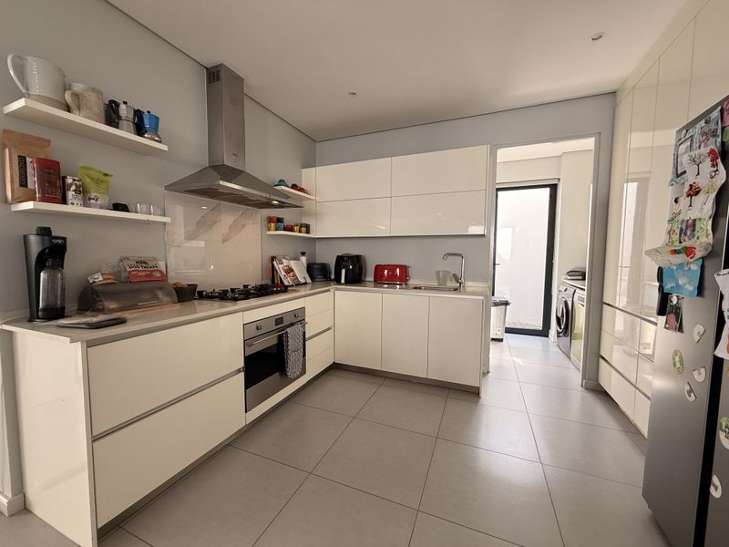 Modern kitchen featuring high-gloss white cabinetry, stone countertops, integrated stainless steel appliances, and tiled flooring, with an adjacent scullery area.