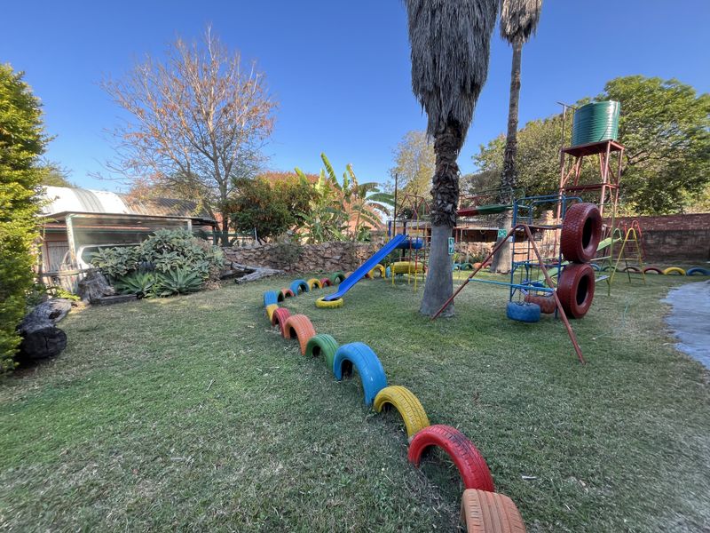 Spacious garden area featuring a built-in playground structure, elevated water tank, and established landscaping with a stone boundary wall.