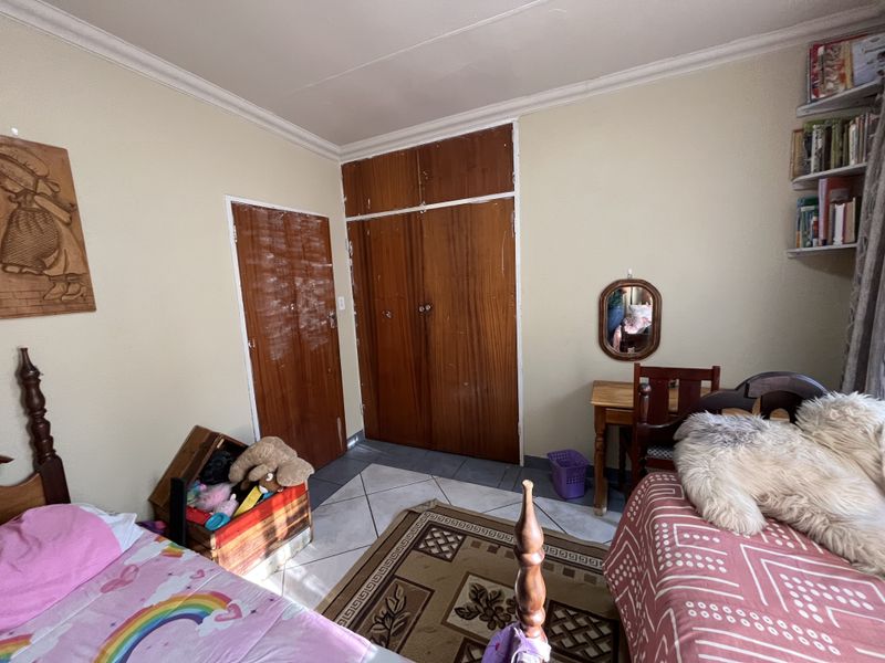 A bedroom featuring tiled flooring, built-in wooden cupboards, and crown molding, offering a functional space with potential for cosmetic updates.