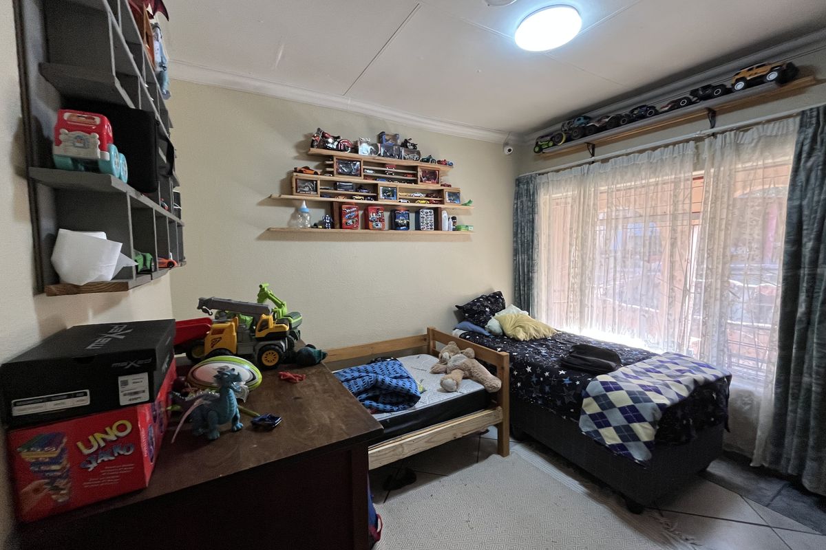 A functional bedroom featuring built-in wall shelving, ceiling lighting, and large windows with curtain rails, providing natural light and storage space.