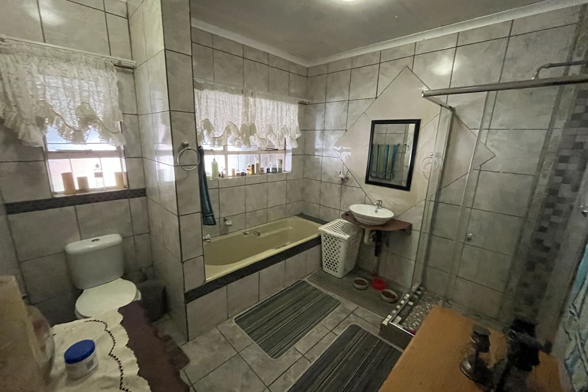 A functional bathroom featuring a built-in bathtub, separate shower enclosure, wall-mounted basin, and toilet, finished with neutral wall and floor tiling.