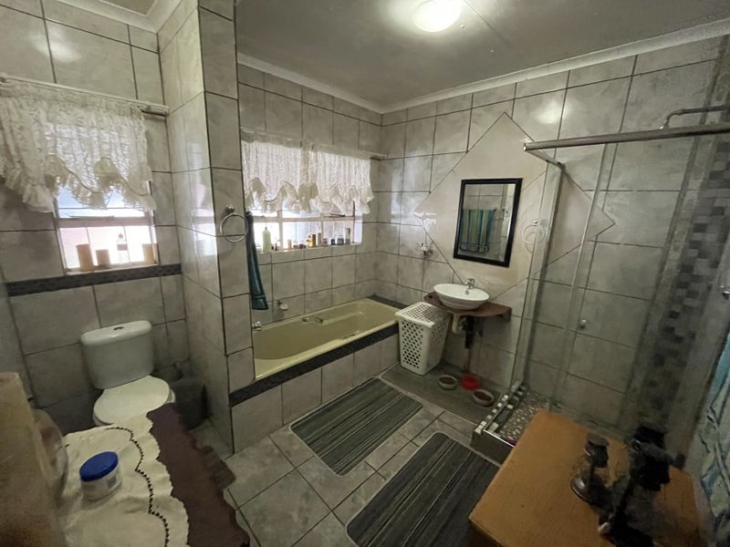 A functional bathroom featuring a built-in bathtub, separate shower enclosure, wall-mounted basin, and toilet, finished with neutral wall and floor tiling.