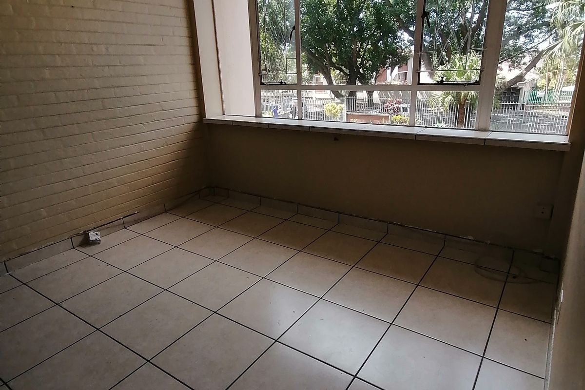 An empty living area featuring tiled flooring, an exposed brick wall, and large windows providing natural light and a view of the exterior.