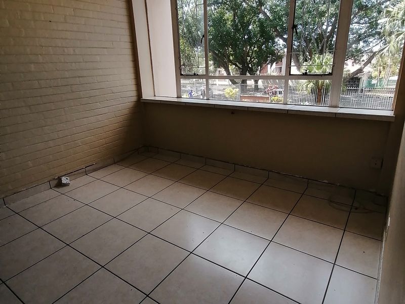 An empty living area featuring tiled flooring, an exposed brick wall, and large windows providing natural light and a view of the exterior.