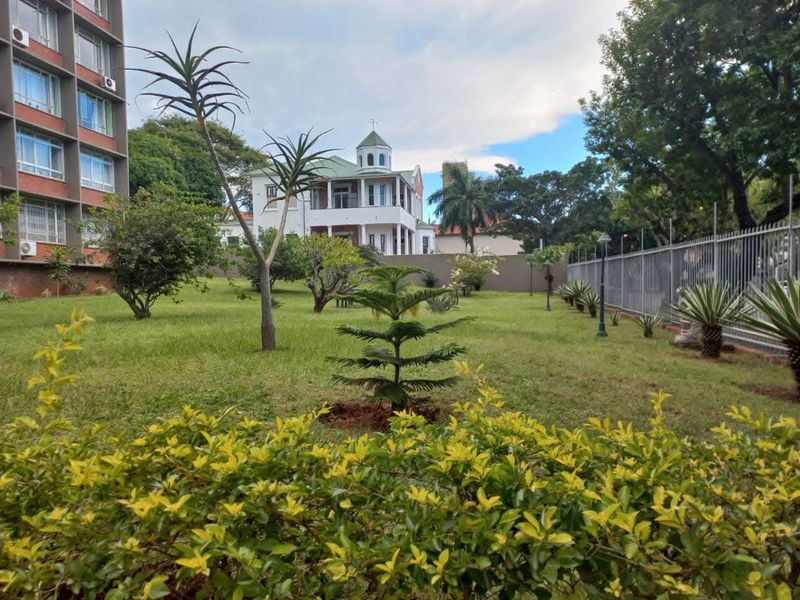 A well-maintained communal garden area featuring a manicured lawn, mature trees, and perimeter fencing, providing a pleasant outdoor space for residents.