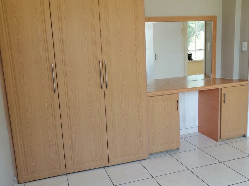 Bedroom featuring built-in wooden cupboards and a matching vanity unit with a mirror, set against tiled flooring.
