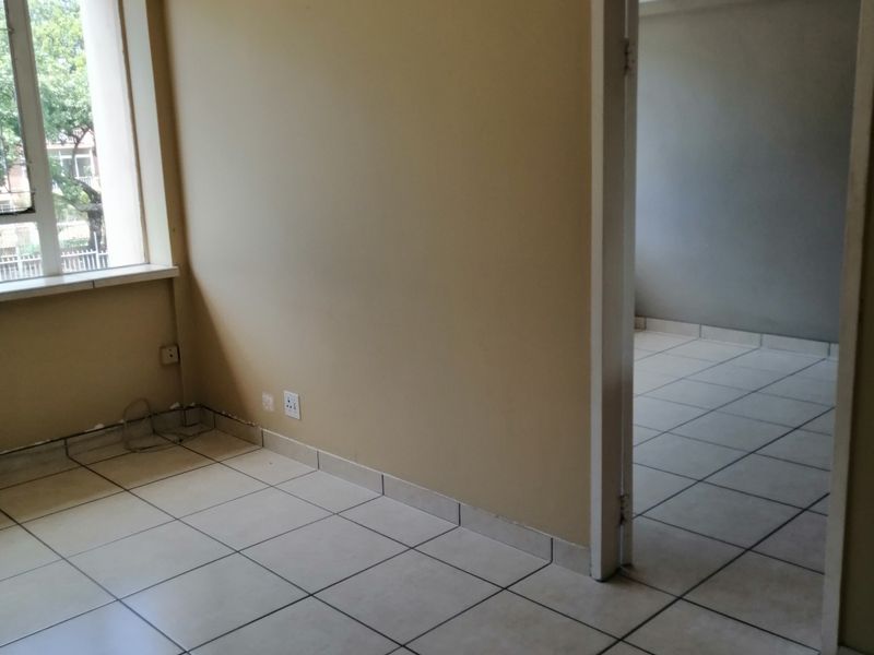 An empty living area featuring neutral ceramic floor tiles, large windows, and direct access to an adjacent room.