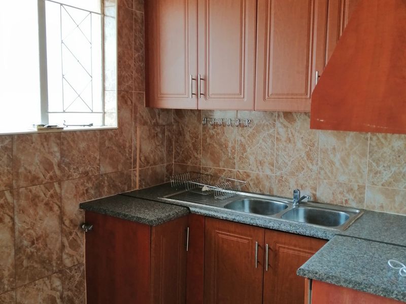 A functional kitchen featuring wood-look cabinetry, granite countertops, a double stainless steel sink, and full-height marble-effect wall tiling.