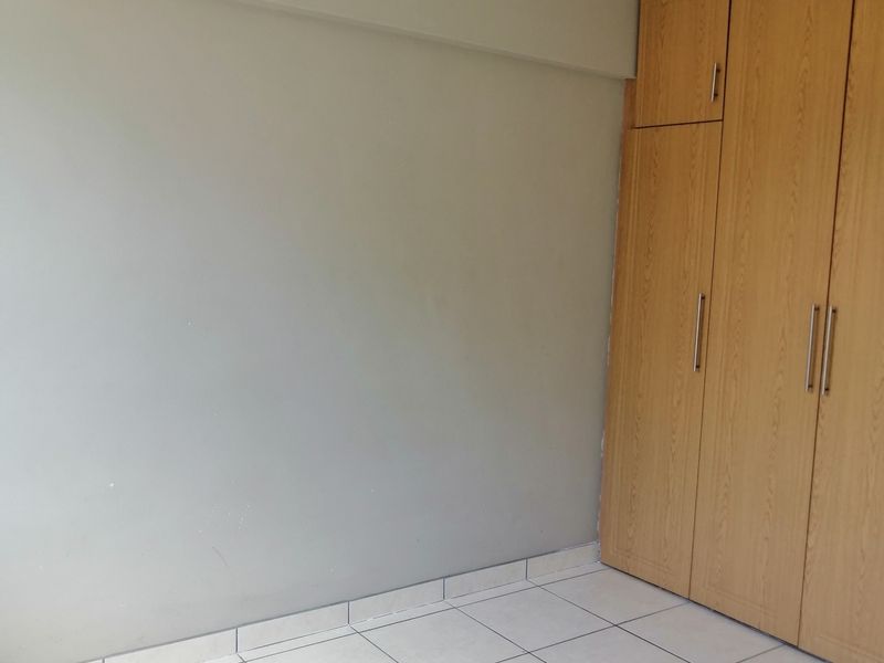 A vacant bedroom featuring light-colored floor tiles, built-in wooden cupboards, and a wall-mounted air conditioning unit.