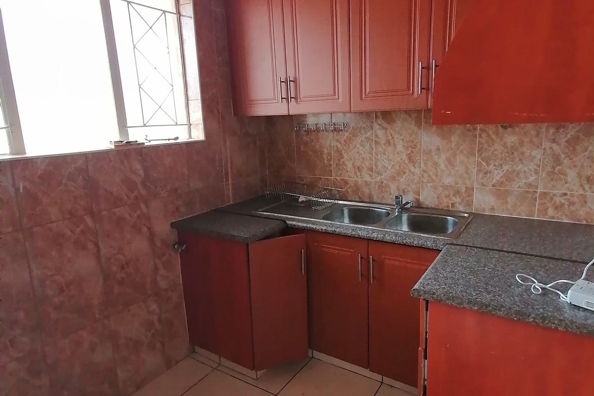 A dated kitchen featuring wooden cabinetry, granite countertops, a double sink, and tiled finishes, requiring cosmetic updates to modernize the space.