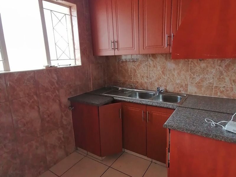 A dated kitchen featuring wooden cabinetry, granite countertops, a double sink, and tiled finishes, requiring cosmetic updates to modernize the space.