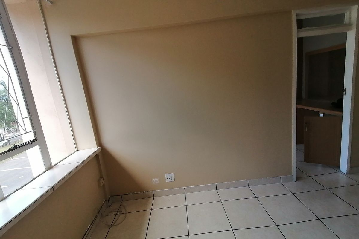An empty bedroom featuring tiled flooring, a window with security bars, and neutral wall finishes, offering a blank canvas for potential renovation.