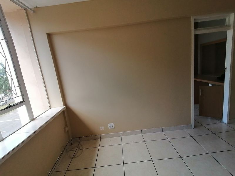 An empty bedroom featuring tiled flooring, a window with security bars, and neutral wall finishes, offering a blank canvas for potential renovation.