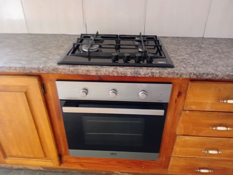 A kitchen section featuring a built-in gas hob, stainless steel oven, granite countertop, and traditional wooden cabinetry with a tiled backsplash.