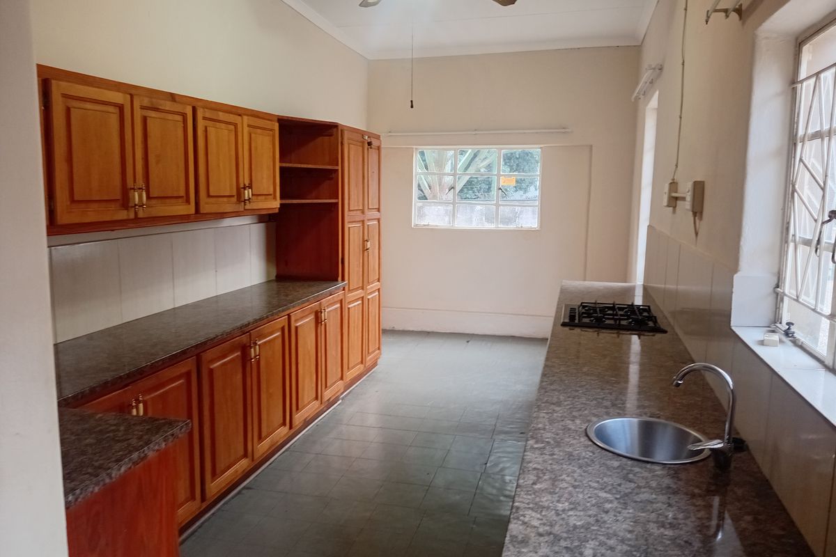 A functional kitchen featuring wooden cabinetry, granite countertops, a built-in gas hob, and a stainless steel sink, offering a clean and spacious layout.