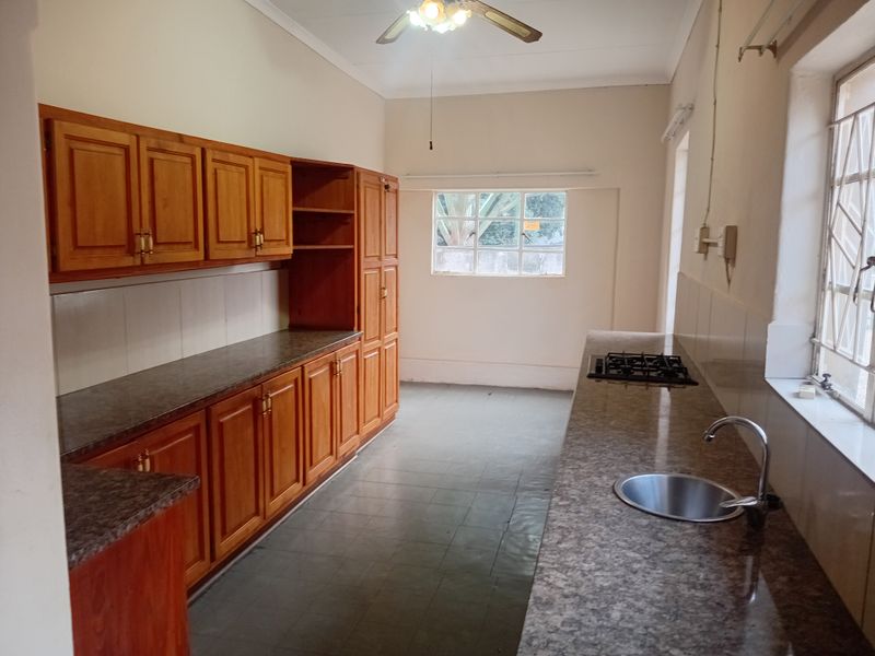 A functional kitchen featuring wooden cabinetry, granite countertops, a built-in gas hob, and a stainless steel sink, offering a clean and spacious layout.