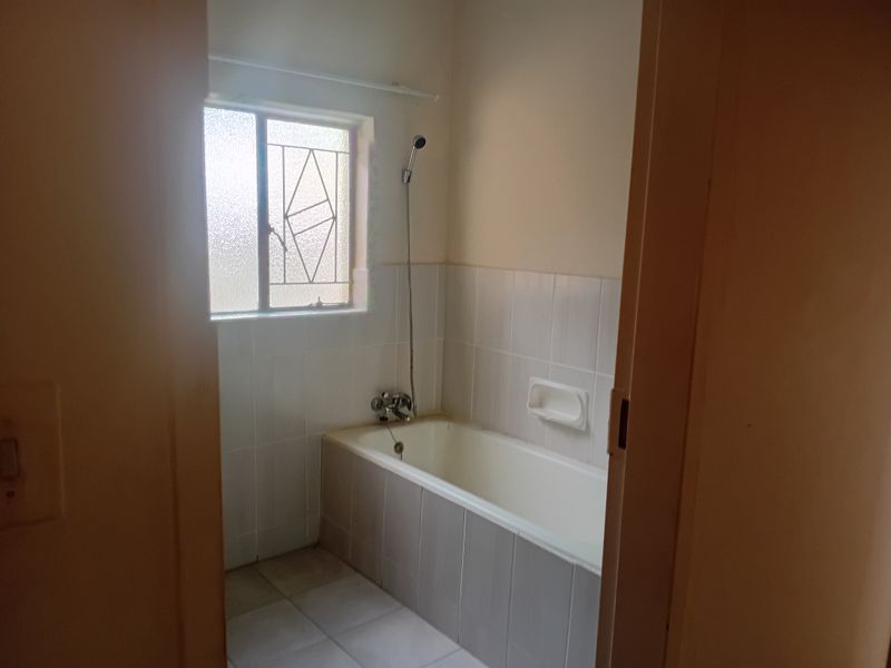 A functional bathroom featuring a built-in bathtub with shower mixer, tiled walls, and a window with security bars.