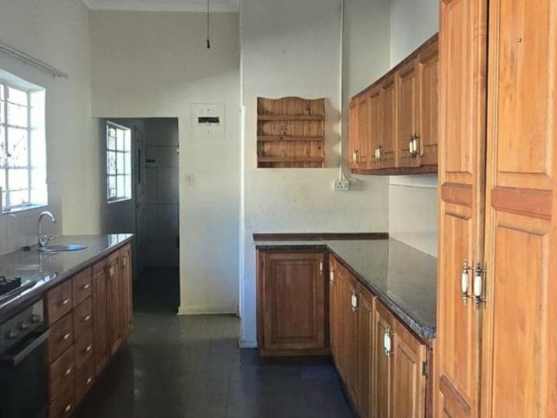 A functional kitchen featuring traditional wooden cabinetry, laminate countertops, built-in oven and hob, and tiled flooring, offering potential for modern updates.