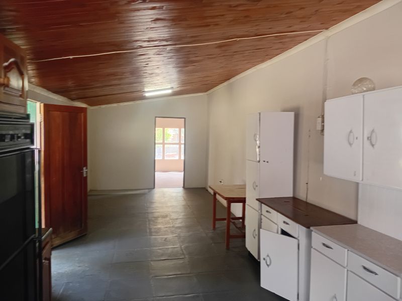 A dated kitchen area featuring timber ceilings, built-in cabinetry, and an integrated oven, offering potential for modernization and renovation.