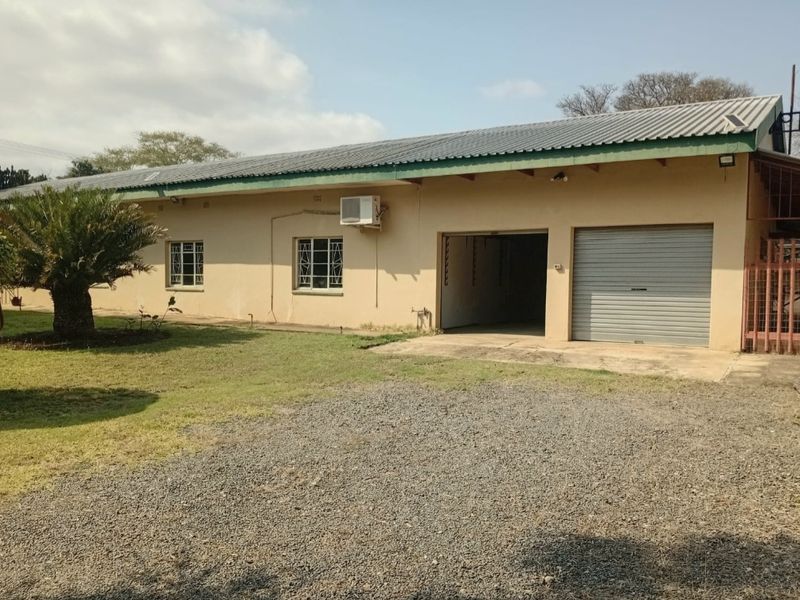 Front exterior view of a single-story house featuring a corrugated metal roof, roller shutter garage door, and gravel driveway.
