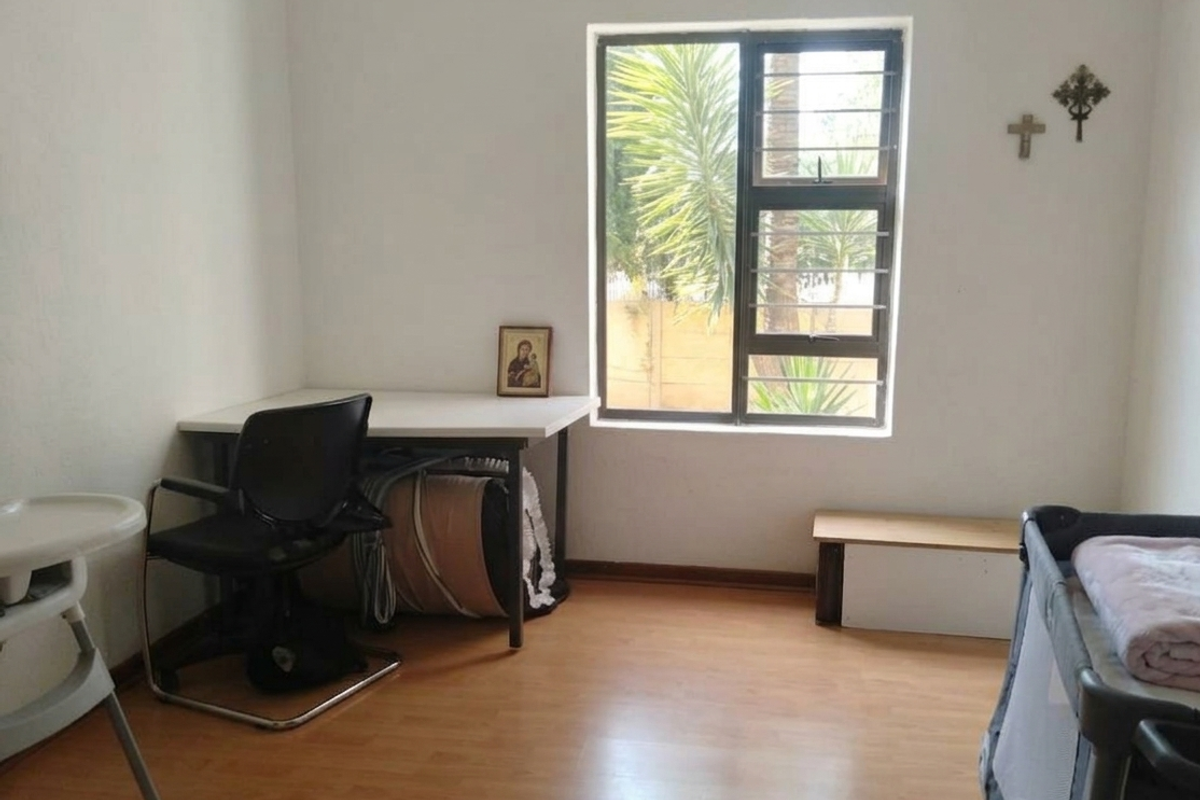 A functional bedroom featuring laminate flooring and a window fitted with security bars, providing natural light and a view of the exterior.